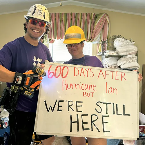two people holding a sign reading 600 days after hurricane ian but we're still here