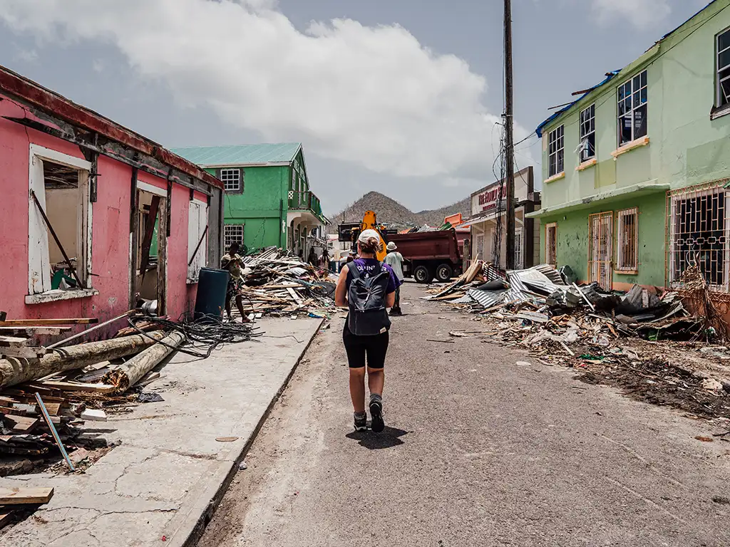 Disaster-relief volunteer walks away from camera through streets sided with destroyed buildings