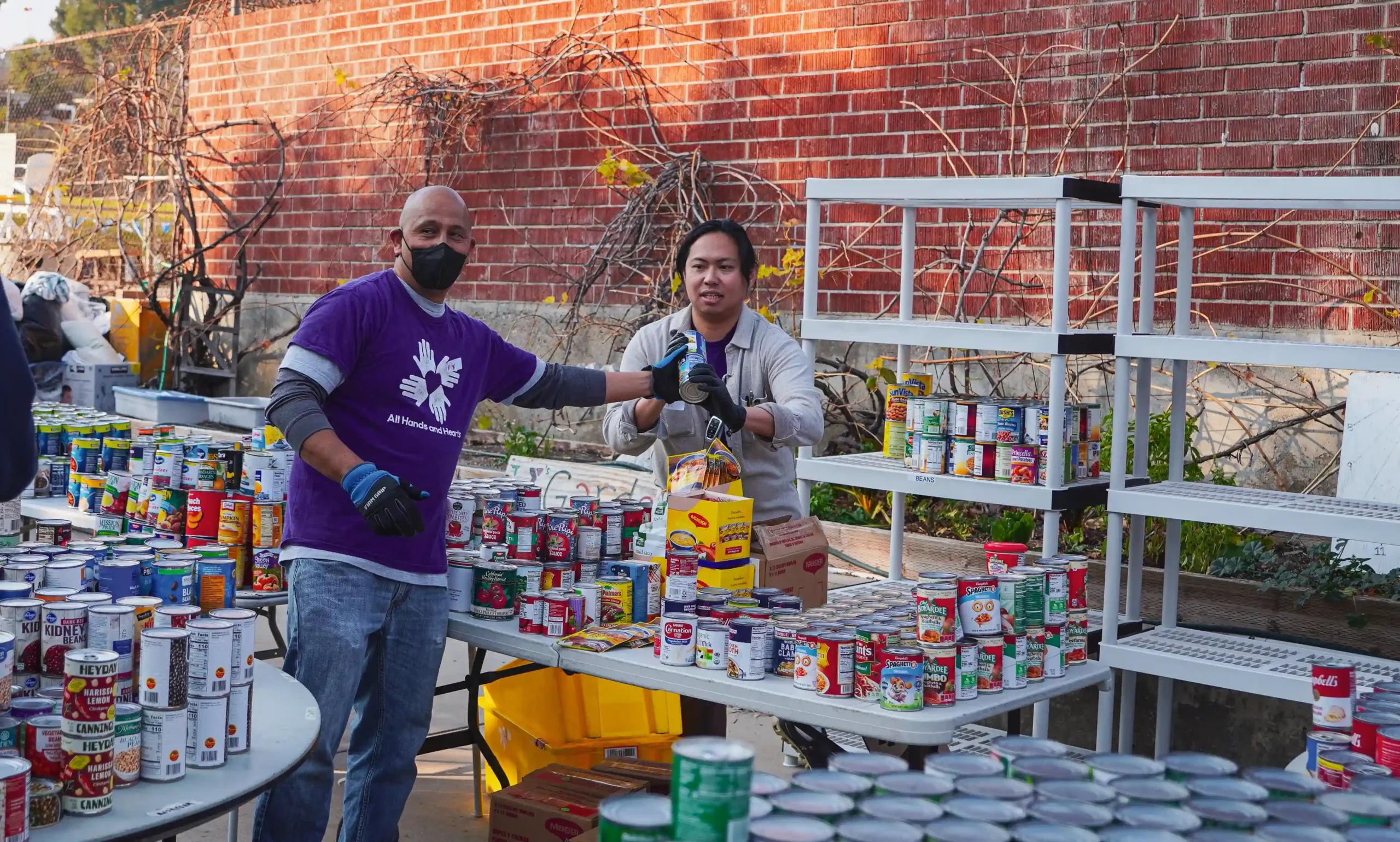 Two All Hands and Hearts volunteers are organizing tinned food outside at a distribution hub
