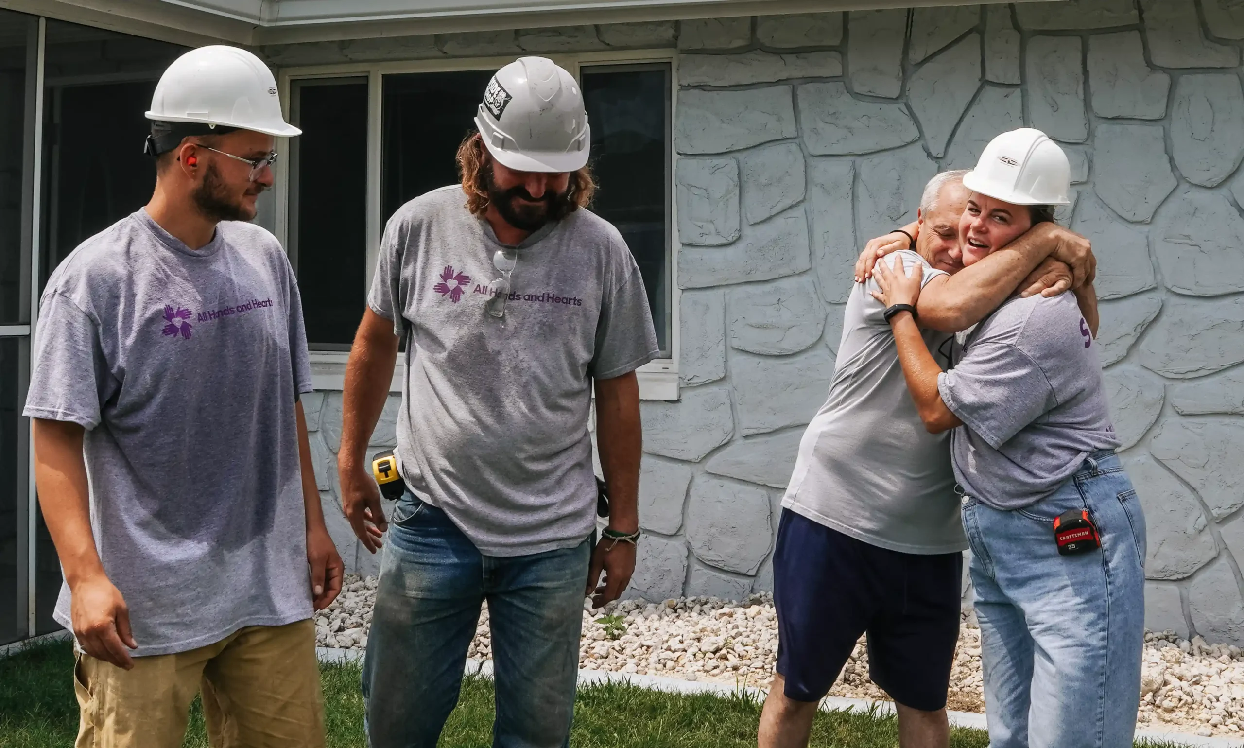 Homeowner hugs an All Hands and Hearts staff member in front of their house, surrounded by three smiling staff members.