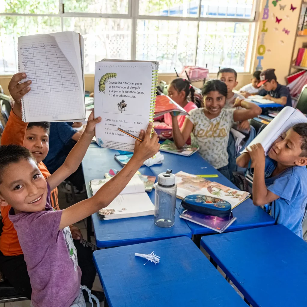 Students in a classroom show their exercise books to the camera