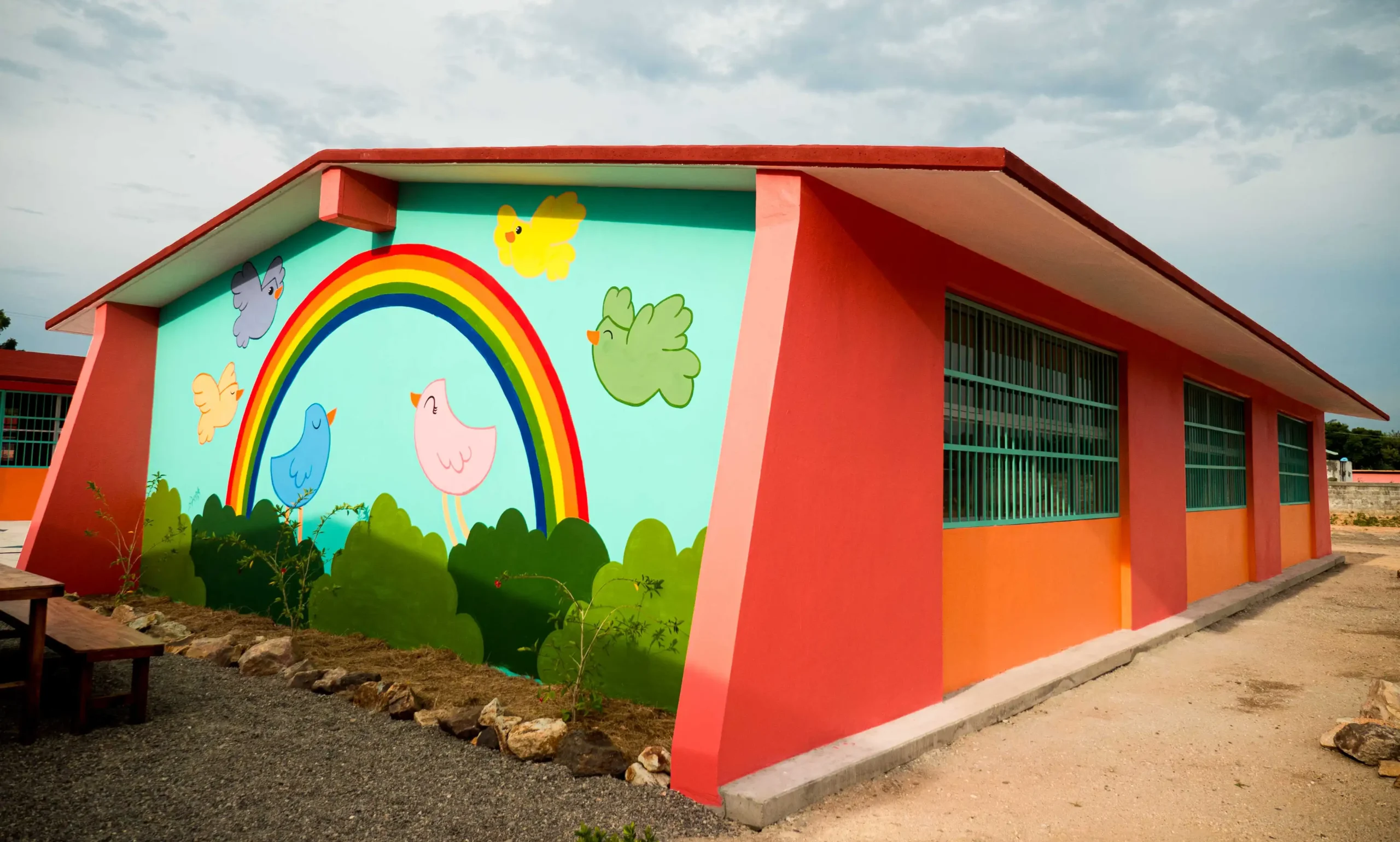 A vibrant. newly built school building with a mural of a rainbow and birds on the outer wall