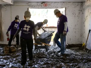 En una habitación dañada por las inundaciones, un grupo de cuatro voluntarios retira los escombros cubiertos de barro.