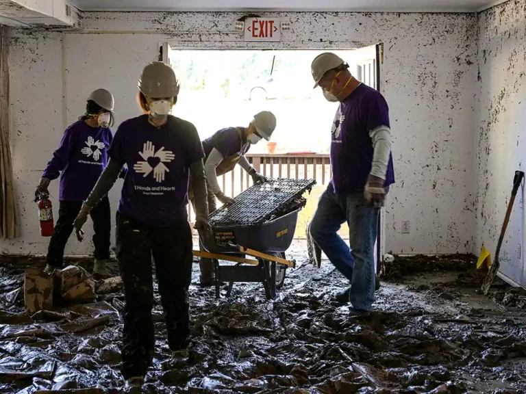 En una habitación dañada por las inundaciones, un grupo de cuatro voluntarios retira los escombros cubiertos de barro.