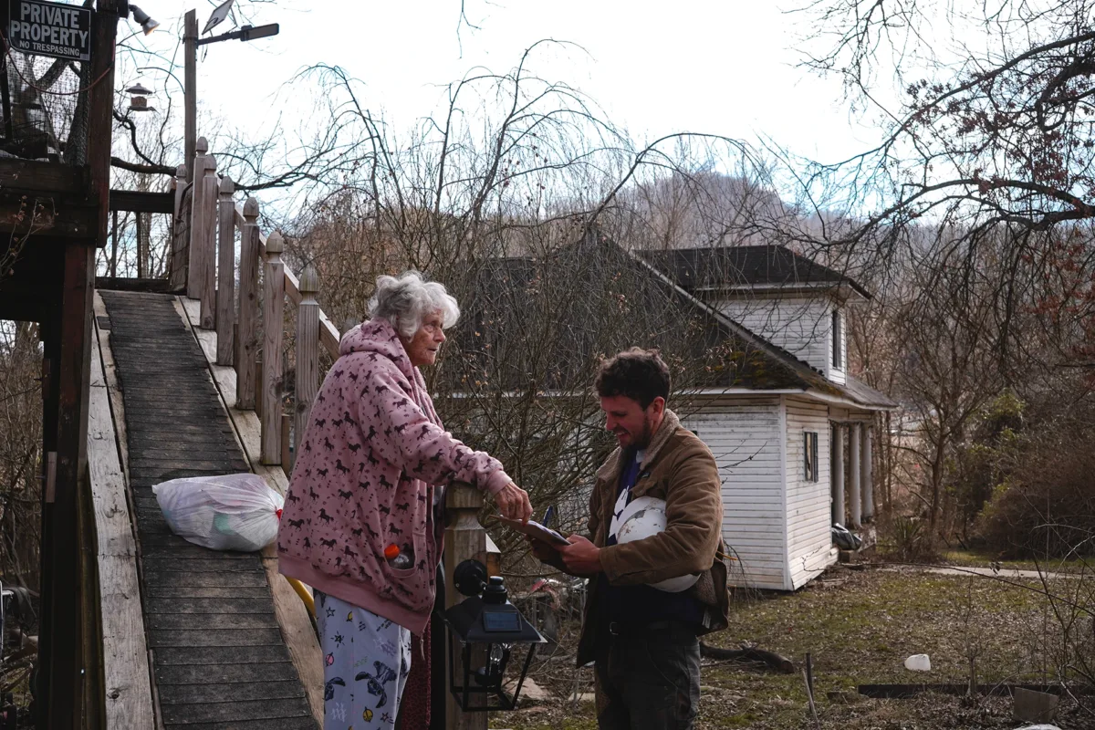 An elderly Kentucky flood survivor speaks with a disaster relief volunteer outside her damaged home during recovery efforts.
