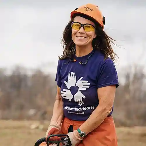 Kentucky tornado relief volunteer smiling in protective gear while holding a chainsaw after debris removal work.