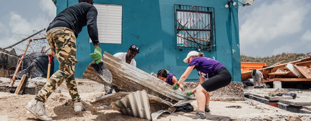 Hurricane Beryl relief volunteers and residents remove heavy debris outside a damaged blue home in Grenada.