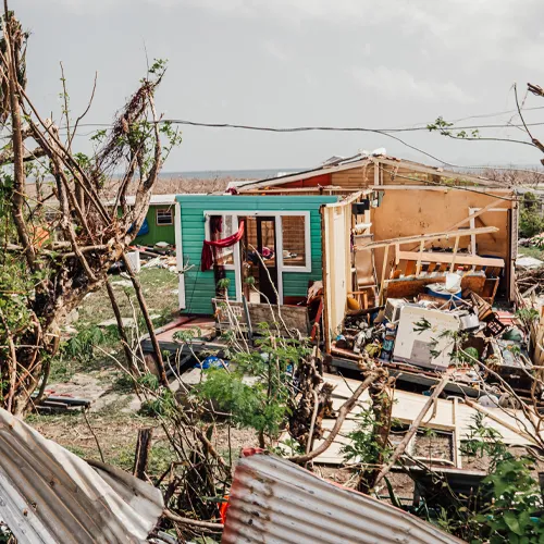 Partially destroyed turquoise house surrounded by scattered debris from Hurricane Beryl in Grenada.