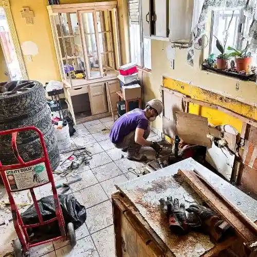 Volunteer wearing a hard hat and purple All Hands and Hearts shirt removes wall panels inside a California flood-damaged home.