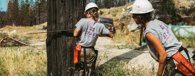 An All Hands & Hearts staff member uses a chainsaw to chop down a burned tree