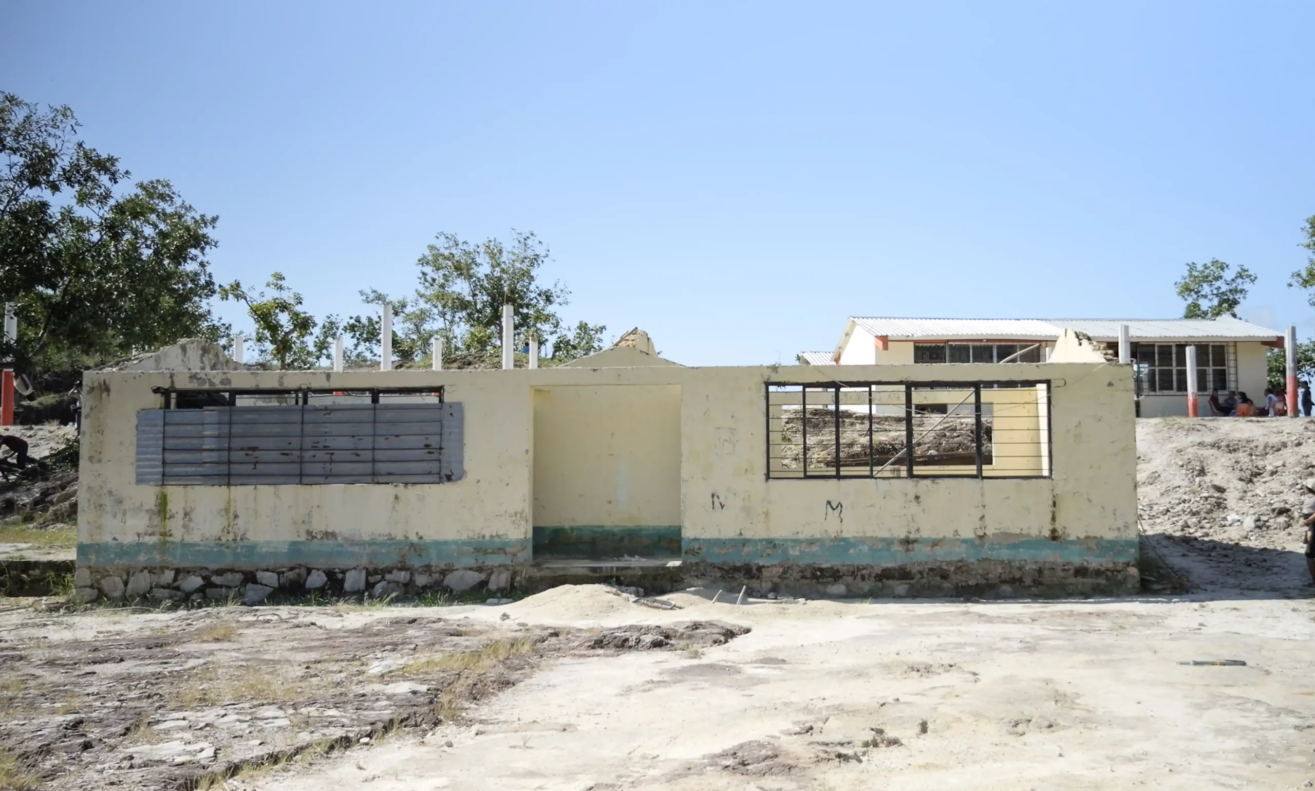 A partially collapsed school building with broken walls and missing roof sections, left in ruins.