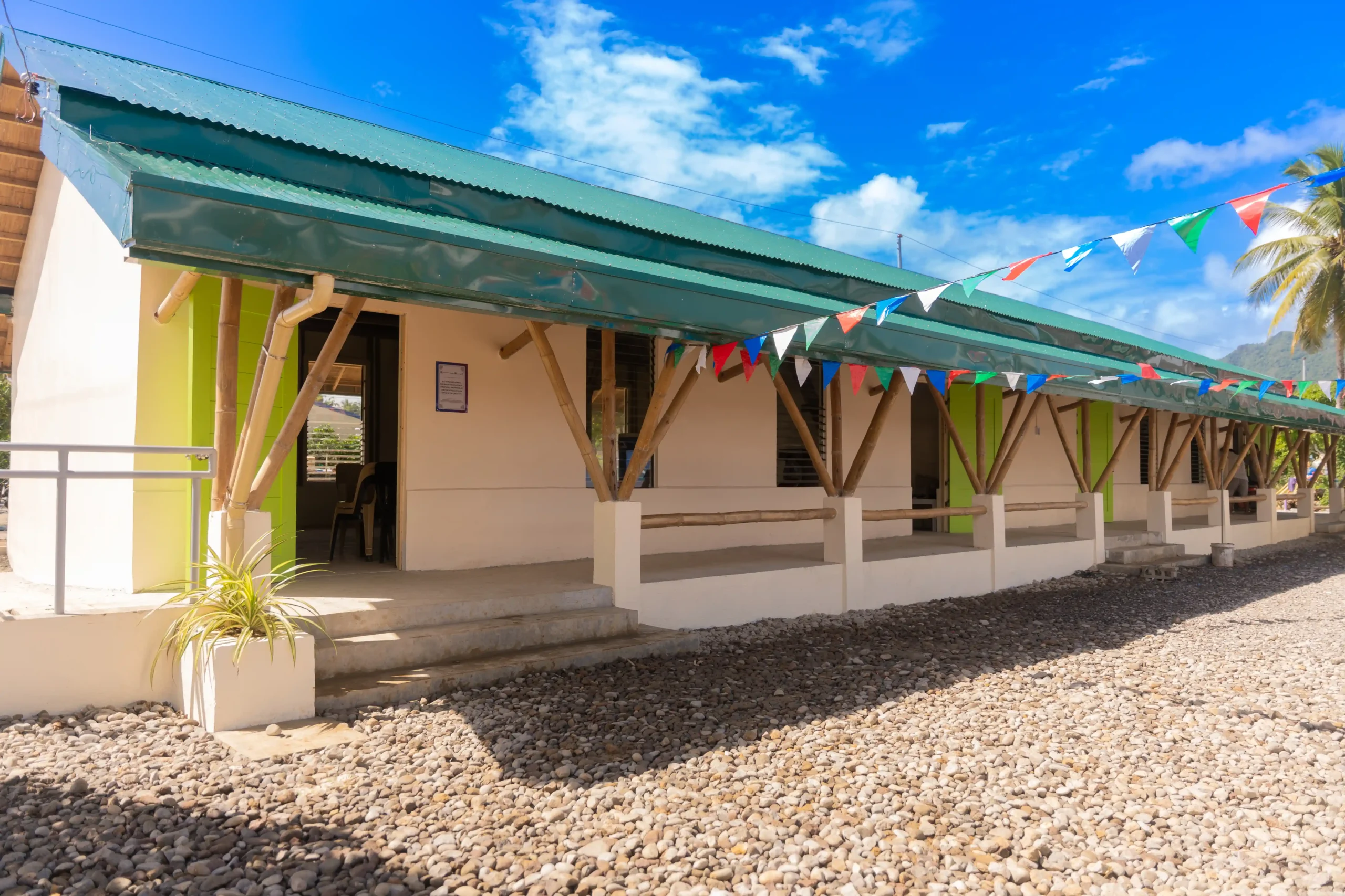 A newly constructed classroom, brightly painted in yellow and blue with colorful bunting hanging from one building to another