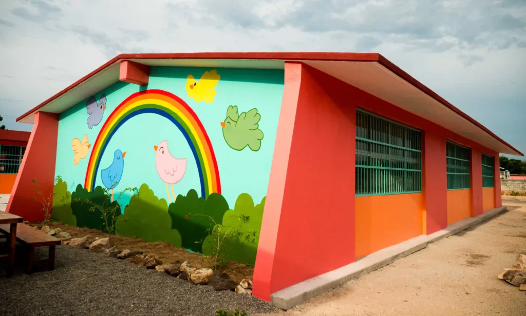 Un vibrante edificio escolar de nueva construcción con un mural de un arco iris y pájaros en la pared exterior.