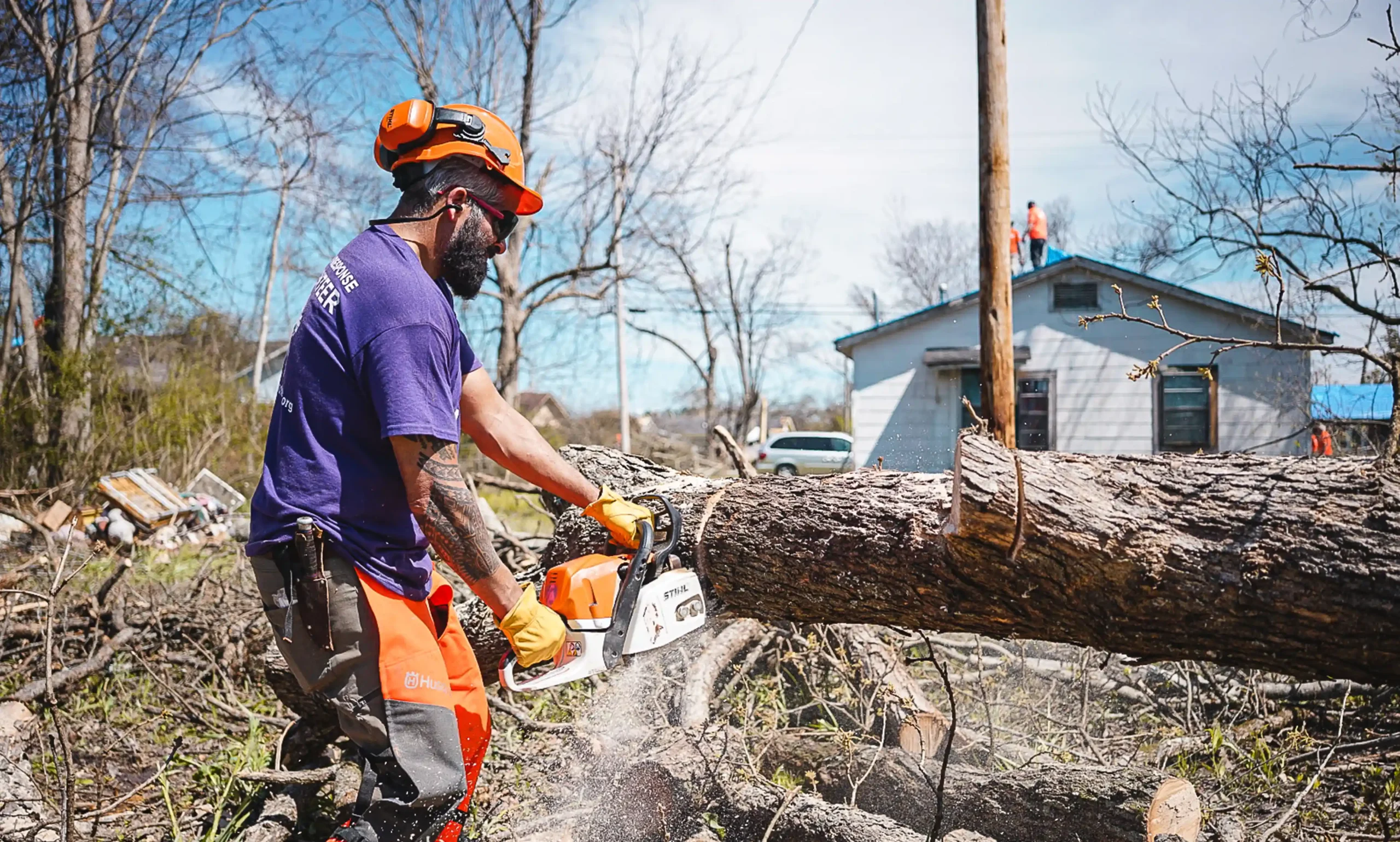 An All Hands and Hearts volunteer with a chainsaw cutting a fallen tree