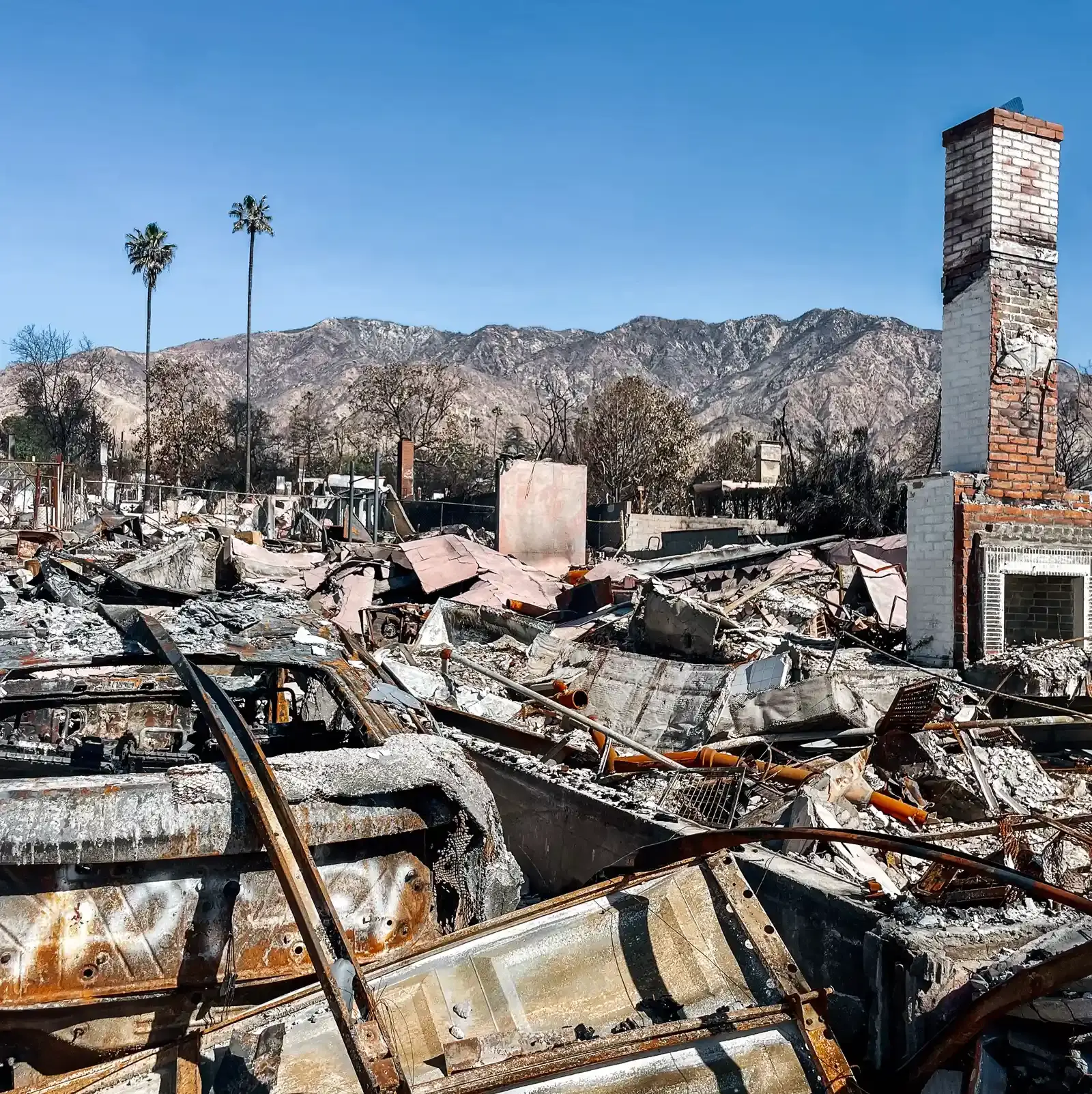 A scene of wildfire destruction, only a brick chimney of a home remains standing amongst ash-covered debris