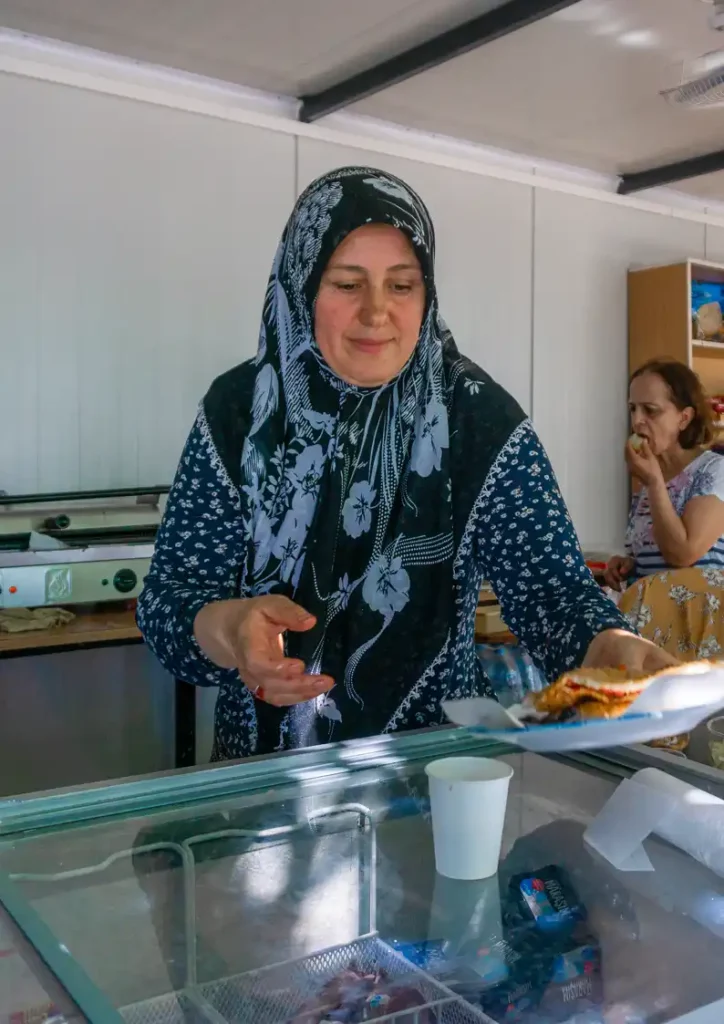 Tulay, passing a plate of food in Kahramanmaraş, Turkiye at the camp AH&H helped improved after the devastating earthquake displaced her community