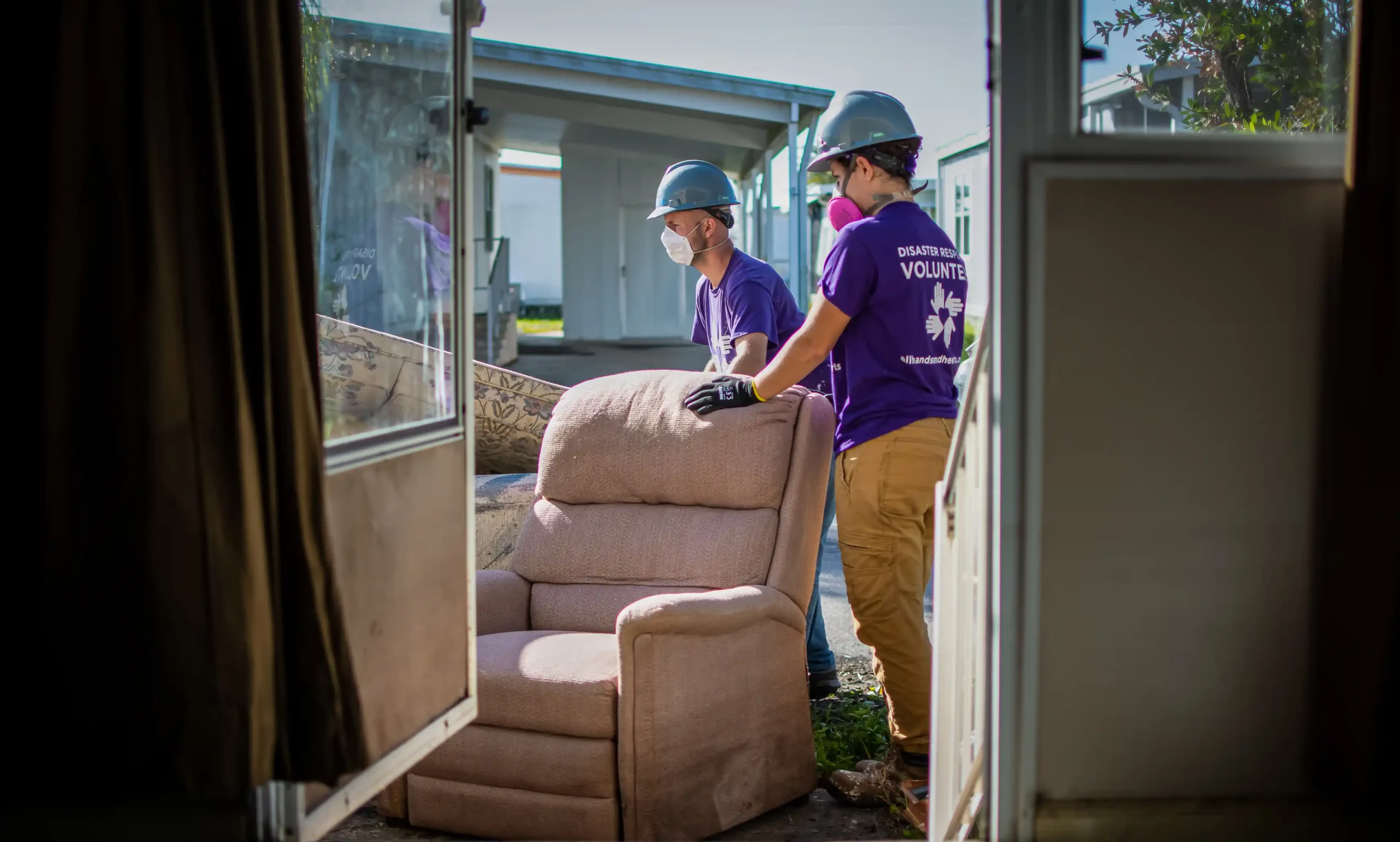 Two All Hands and Hearts volunteers moving a chair from flood-damaged home