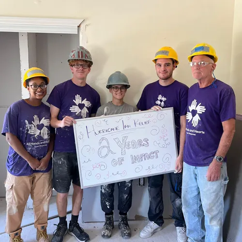 Hurricane Ian relief volunteers in Florida hold a sign marking two years of recovery impact.