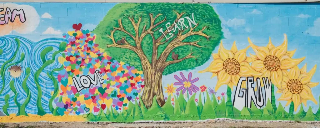 Colorful community mural in Florida created after Hurricane Michael, featuring ocean waves, a tree, sunflowers, and the words “Love, Learn, Grow, Dream.”