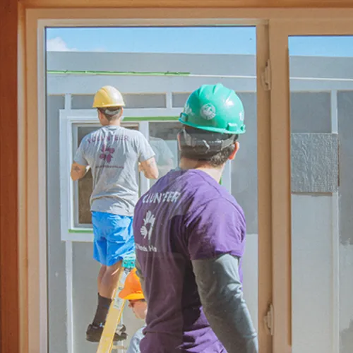 Maui wildfire relief volunteers in hard hats install new windows in a community housing project.