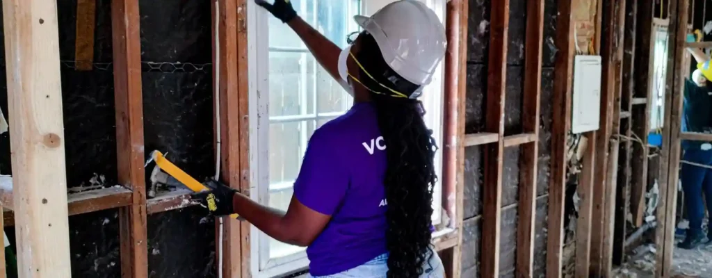 Volunteer in protective gear works inside a flood-damaged California home, repairing the interior walls after severe flooding.