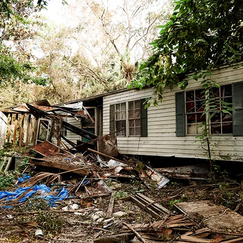 Florida home severely damaged by Hurricane Idalia, with collapsed siding and scattered debris in the yard.