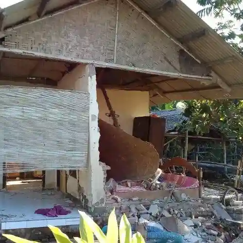 A small house with bamboo walls and a collapsed interior wall, exposing damage and debris from the Indonesia earthquake.
