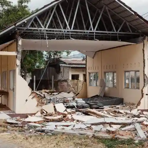 A house with cracked and crumbling walls, showing exposed interior rooms and heavy structural damage.