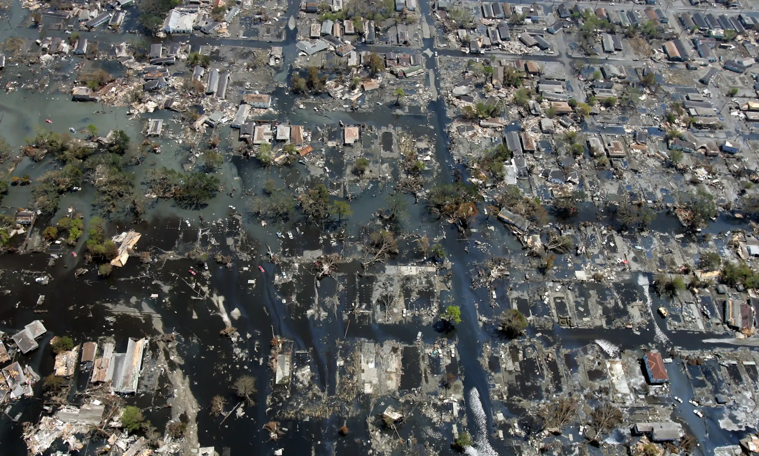 An aerial view of a flooded neighborhood after Hurricane Katrina, showing rows of submerged homes, debris, and streets covered in water and mud, reflecting large-scale devastation.