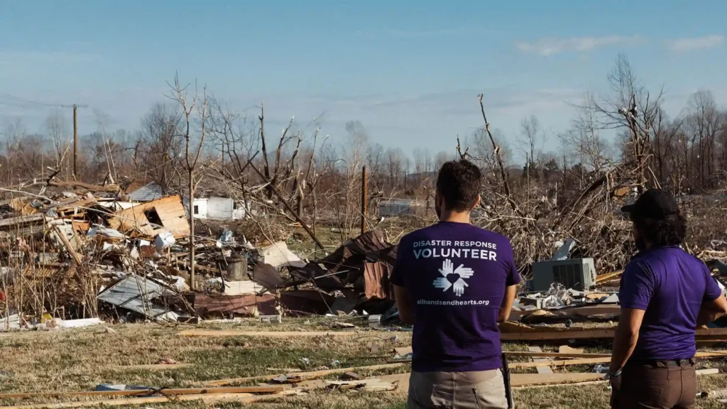 All Hands and Hearts disaster response volunteers surveying widespread tornado destruction in Kentucky with collapsed homes and broken trees.