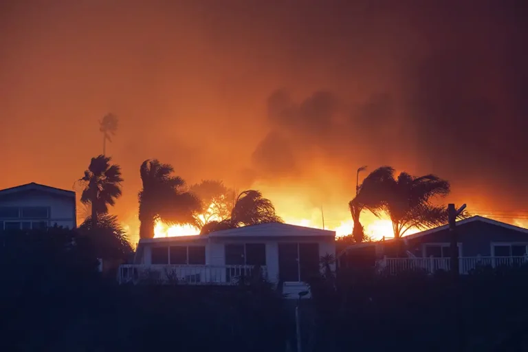 A home engulfed in flames as a wildfires rages behind, the whole sky bright orange