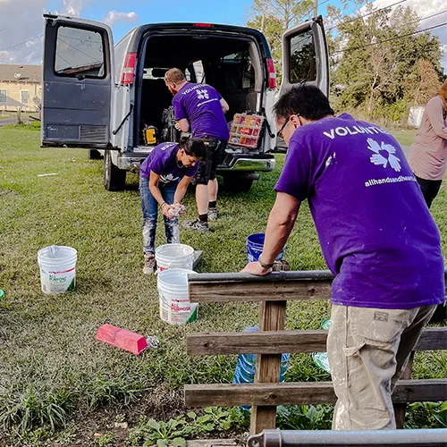Volunteers in purple All Hands and Hearts shirts unload supplies from a van and prepare buckets for disaster relief work.