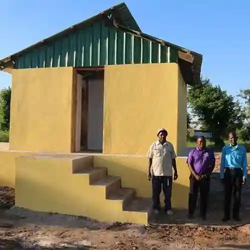 Three men stand in front of a newly constructed yellow building with green roof panels in Mozambique.
