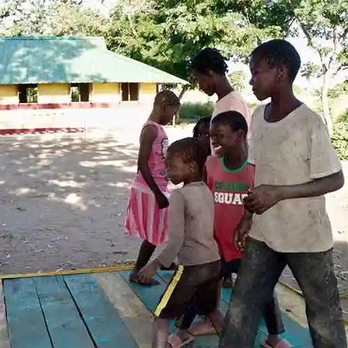 A group of children play together on a colorful wooden platform near a school building in Mozambique.
