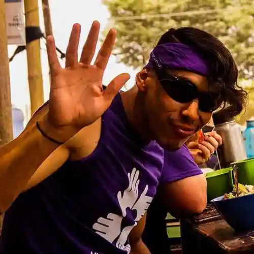 Una voluntaria con una camiseta morada All Hands and Hearts sonríe y saluda a la cámara durante una pausa para comer.