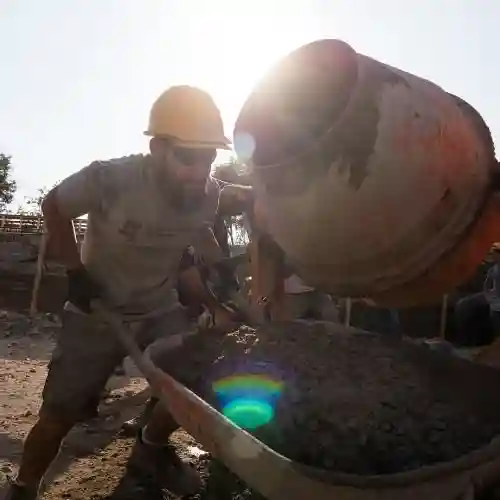 Voluntario con casco y guantes vierte hormigón mezclado en una carretilla en una obra.