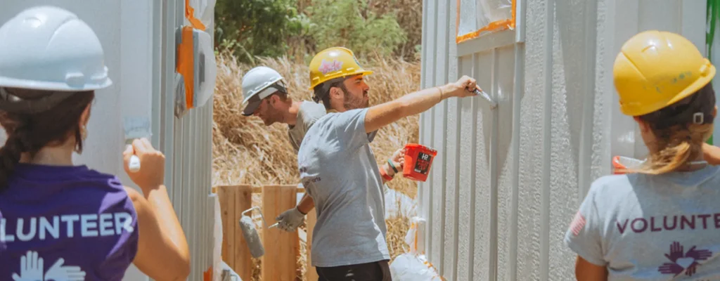 Volunteers in Maui paint temporary housing units as part of wildfire recovery efforts.