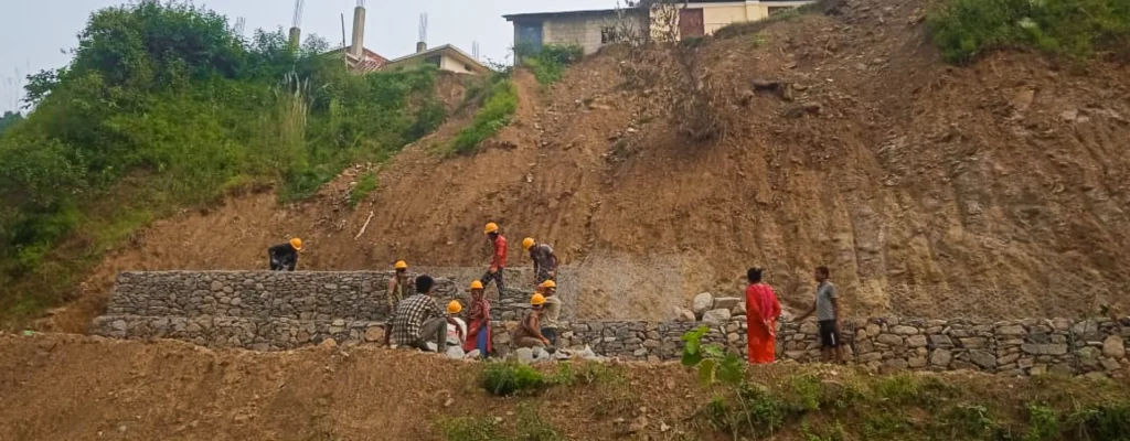 Voluntarios con cascos amarillos refuerzan un muro de contención de piedra en una ladera empinada tras los daños causados por el monzón en Nepal.