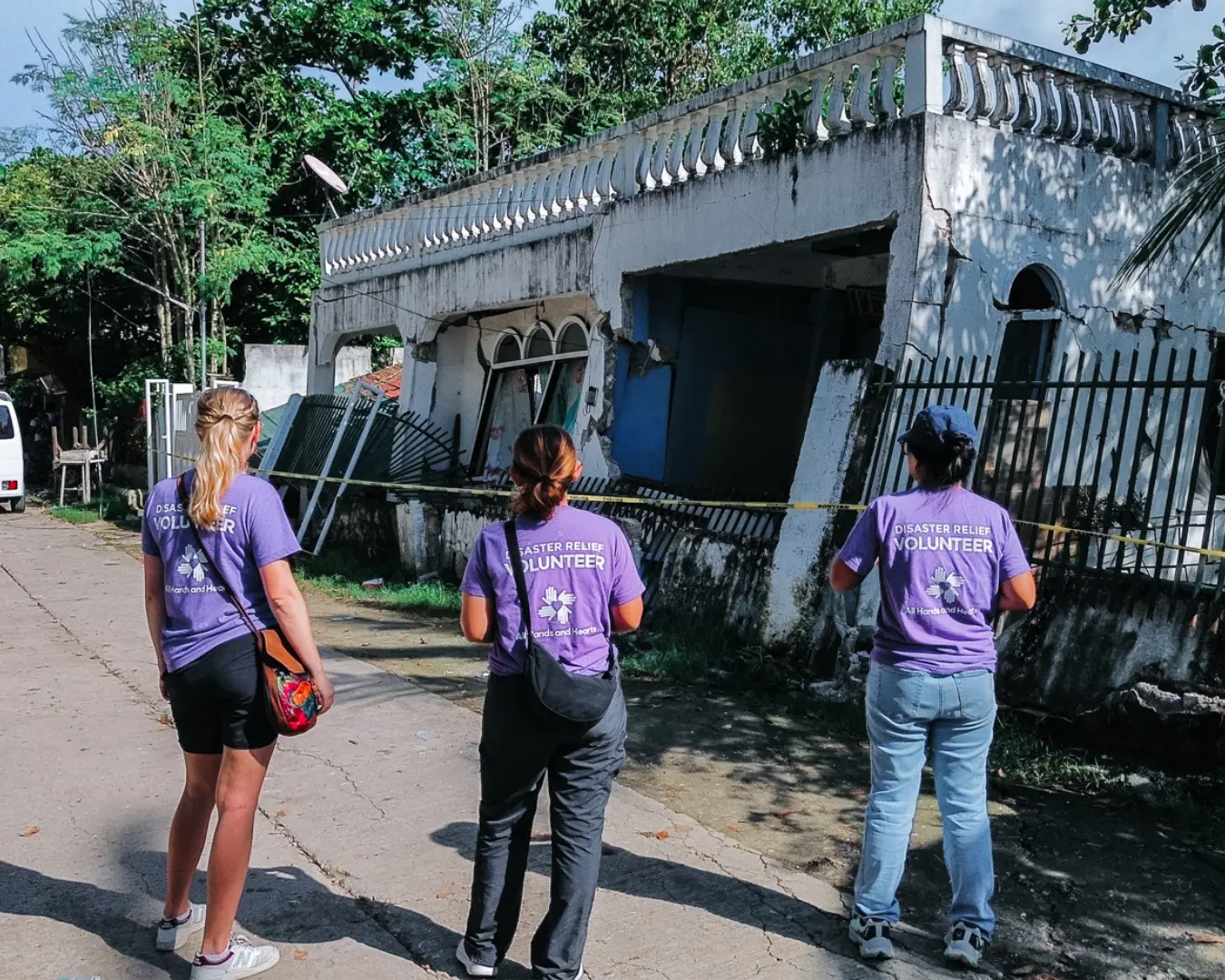 Three individuals stand in front of damaged building