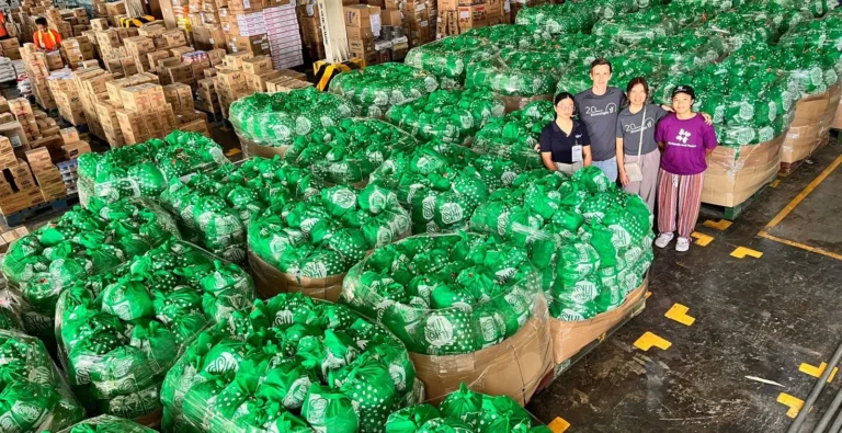 Four individuals stand amongst hundreds of bags containing relief items