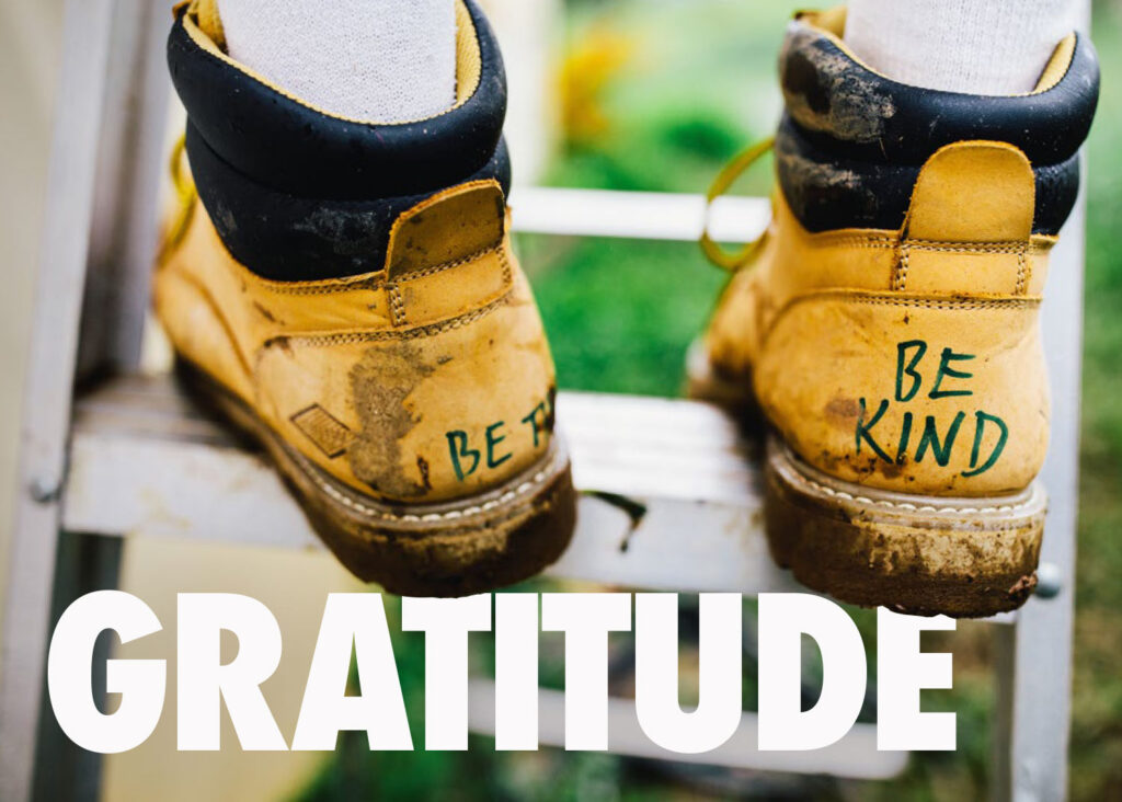 Image of work boots with the words Be Kind written on the back and the word Gratitude overlayed on the image
