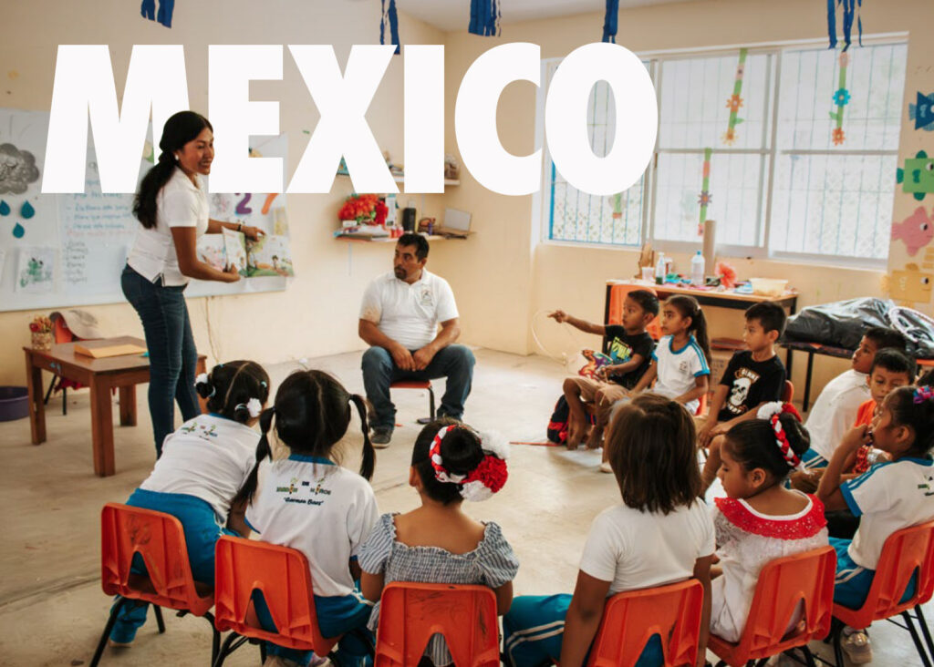 Image of children in a classroom seated around a teacher reading a story.